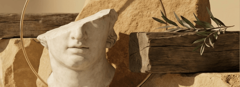 Fragmented classical marble bust surrounded by natural stone, rough wood, a golden ring, and an olive branch, evoking ancient beauty.